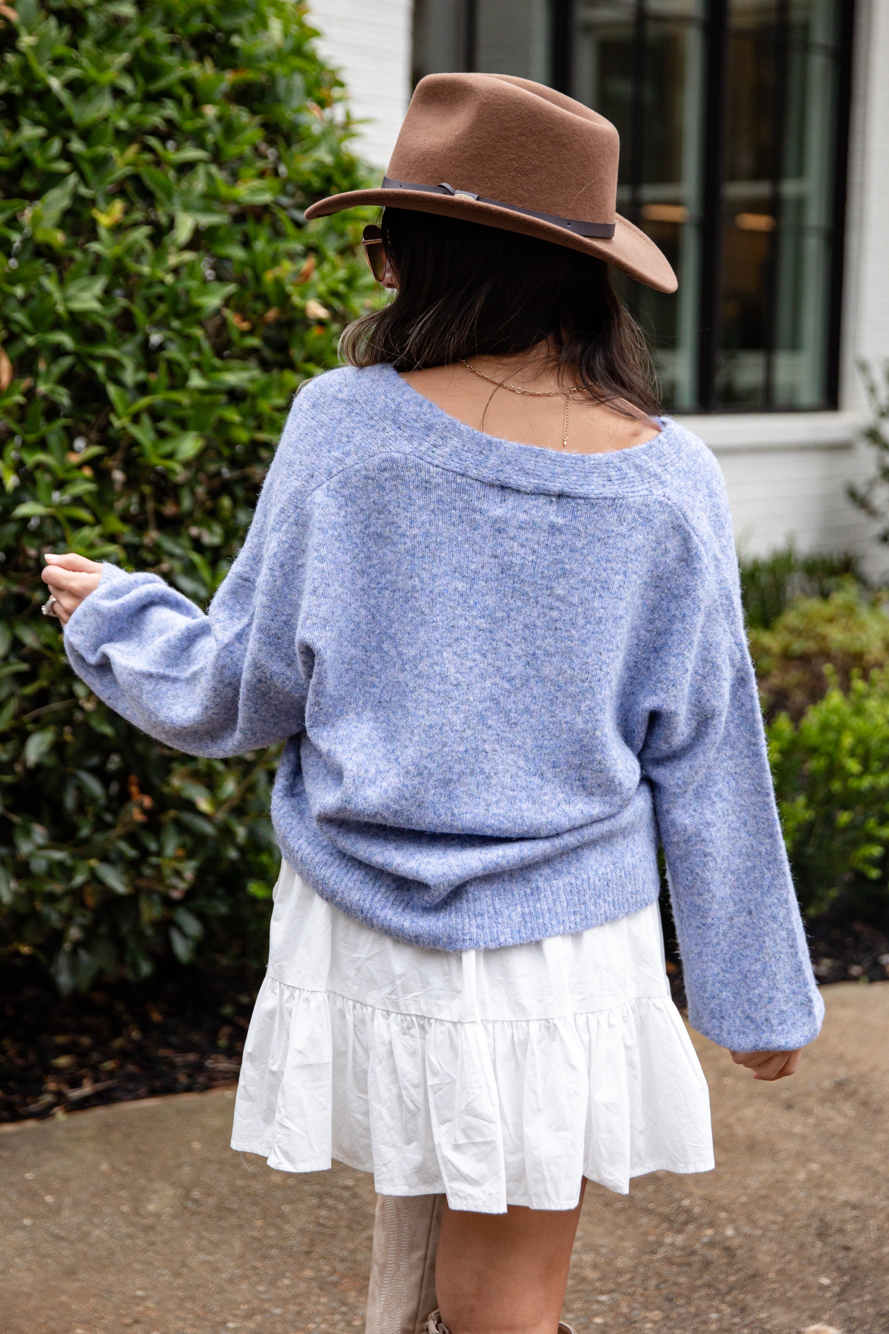 Person wearing a blue sweater and white skirt with a brown hat outdoors.