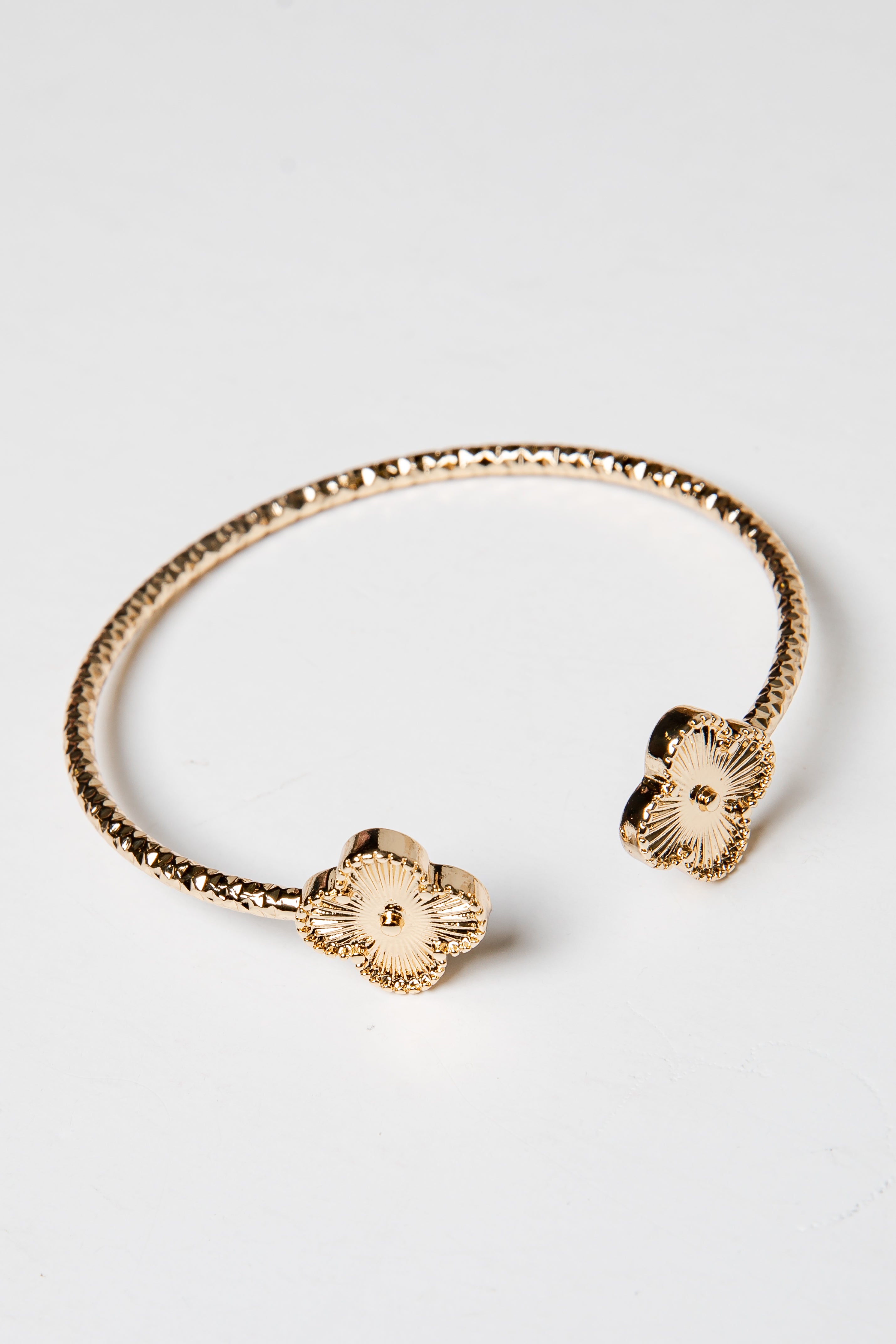 Gold bracelet with floral ends on a light gray background