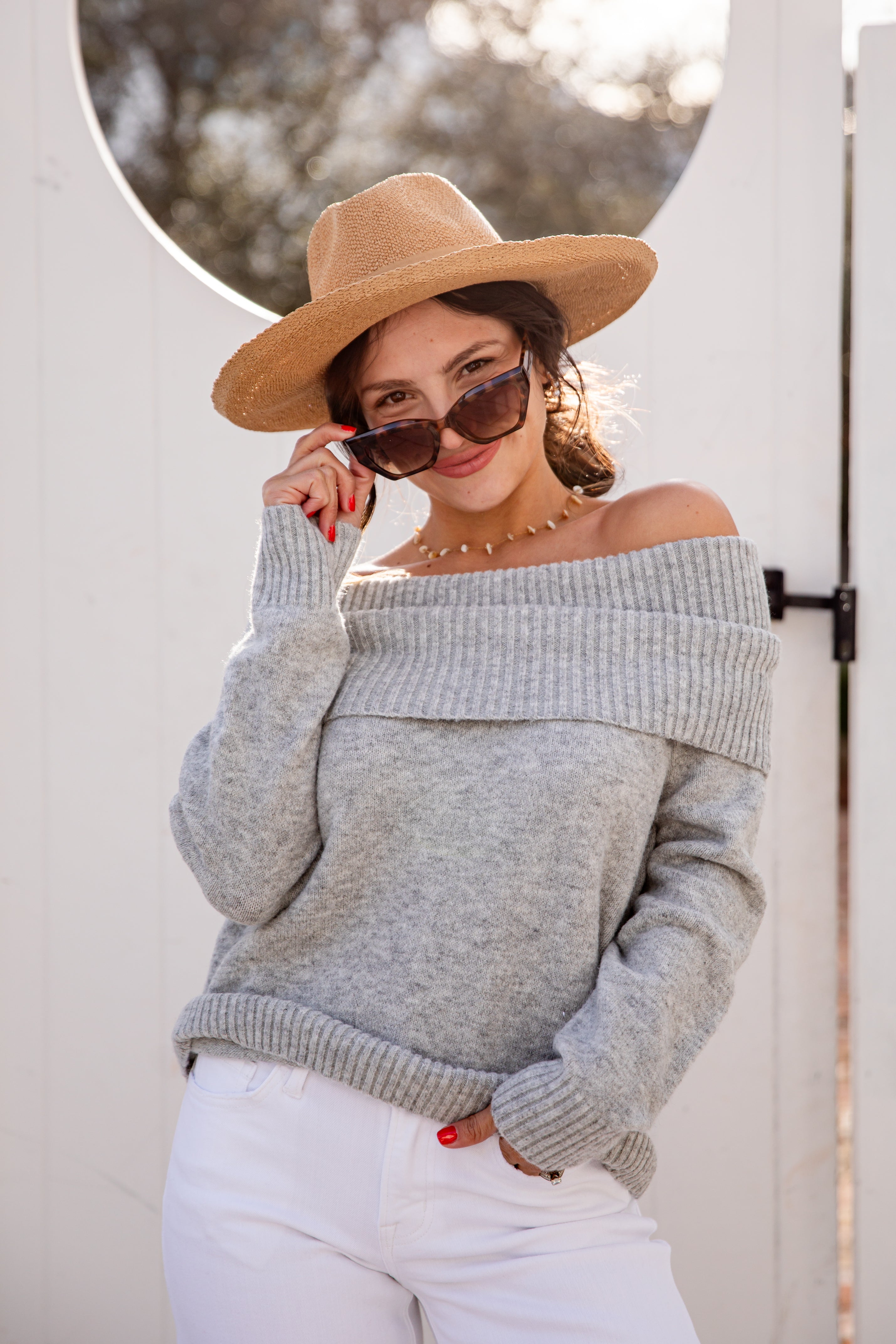 Woman wearing a gray off-shoulder sweater and beige hat, standing outdoors.