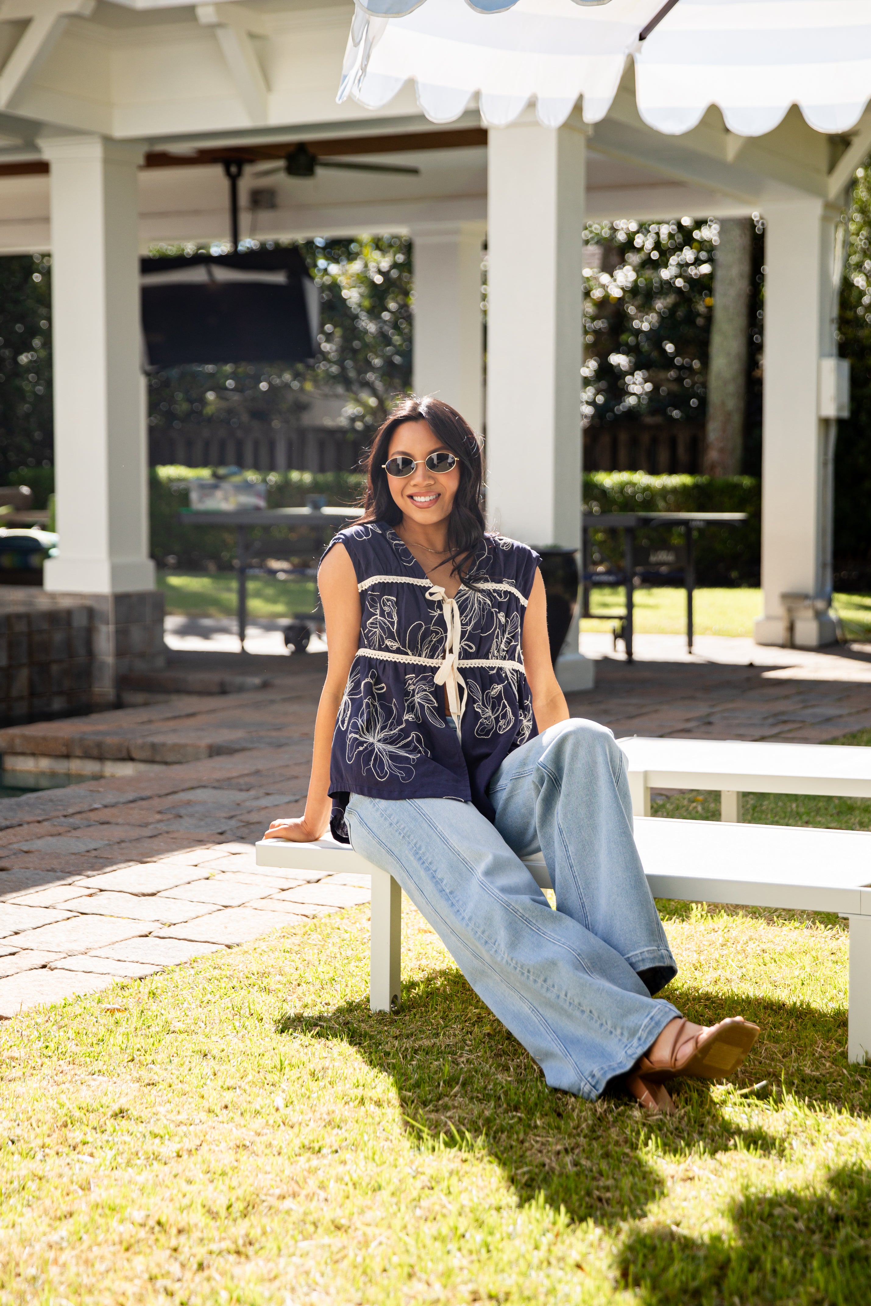 Woman sitting on a bench in a park-like setting with a gazebo in the background.