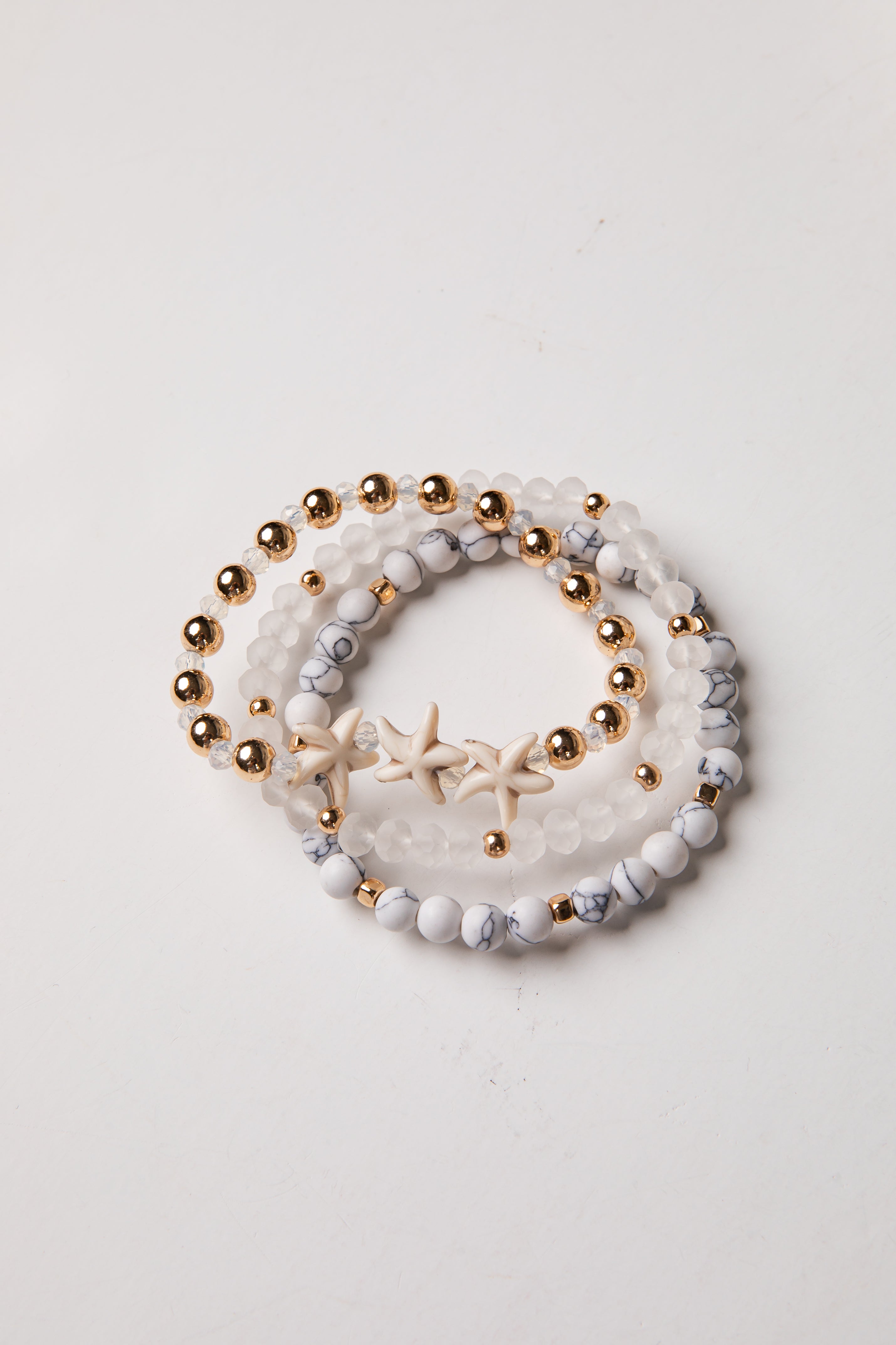 Set of three beaded bracelets with gold beads and starfish charm on a light background