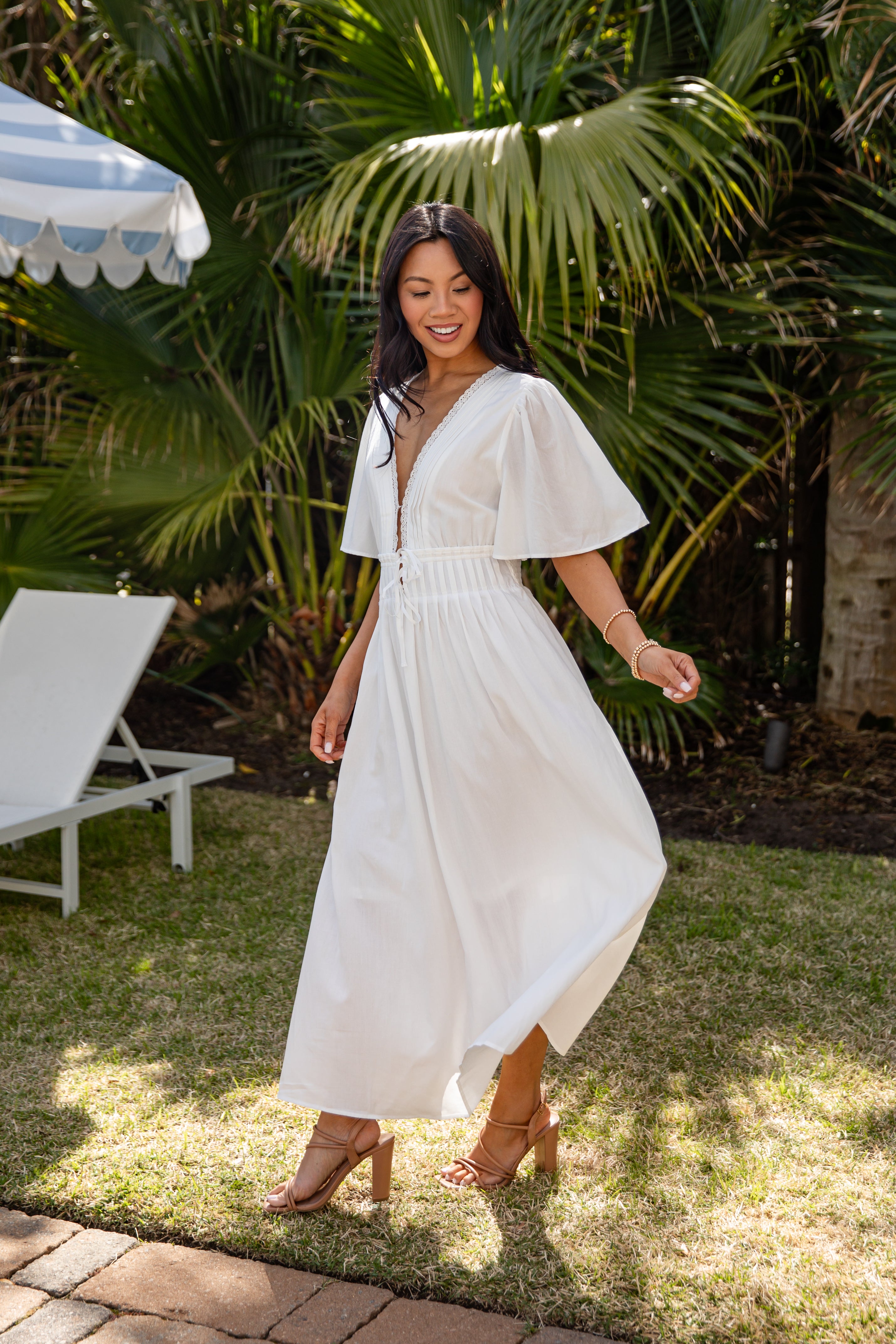 Woman in a white dress standing outdoors with palm trees in the background