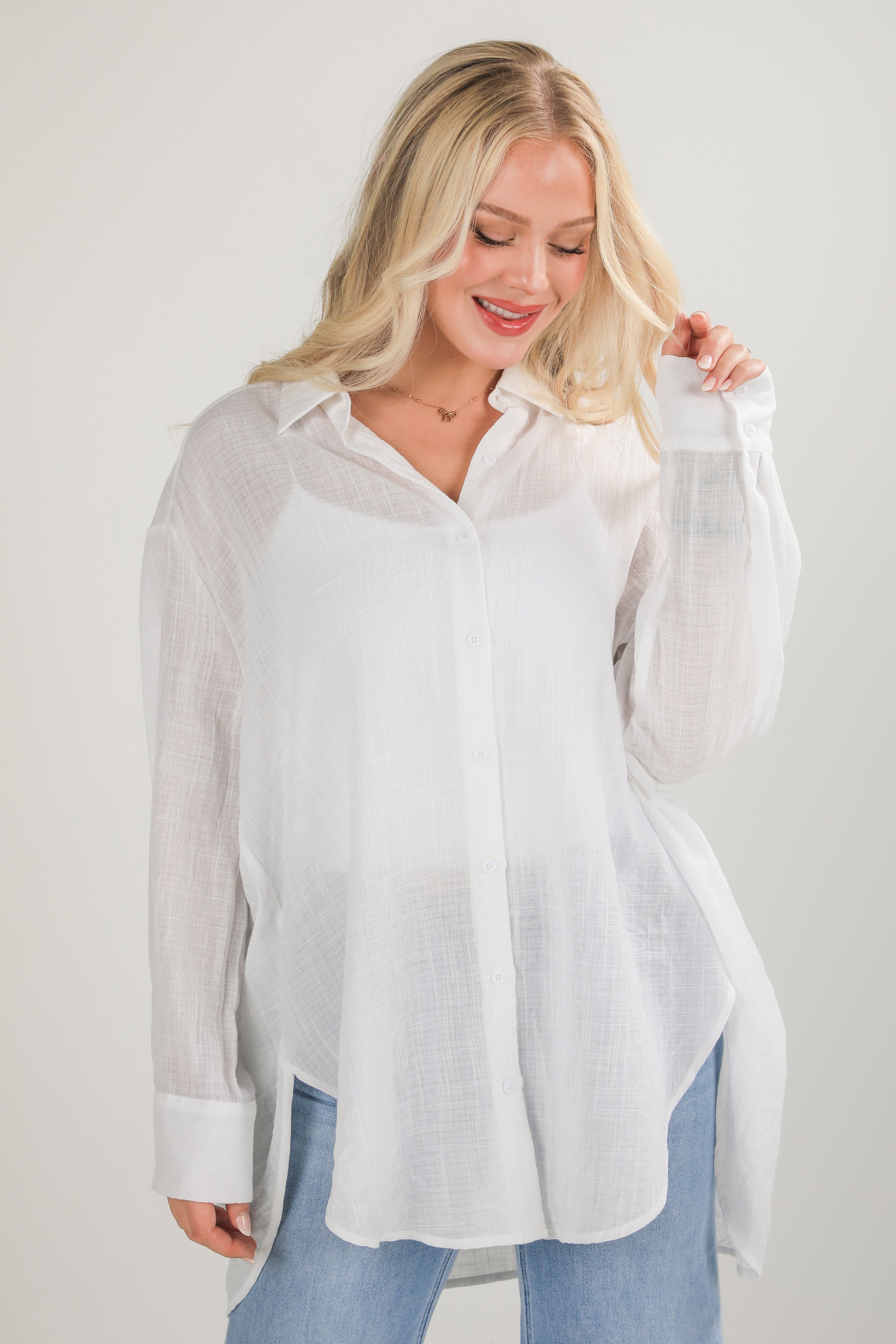 Woman wearing a white button-up shirt with sheer sleeves against a plain background