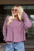 Woman wearing a purple sweater and blue jeans in a living room setting.