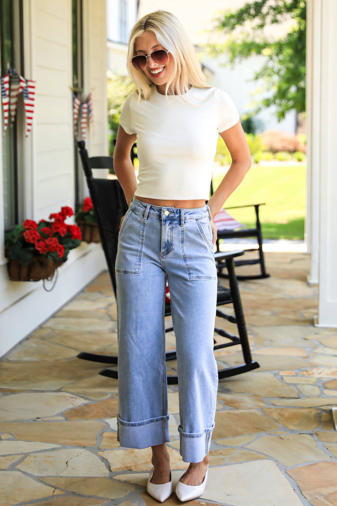 Woman in white crop top and blue jeans standing on a stone porch.