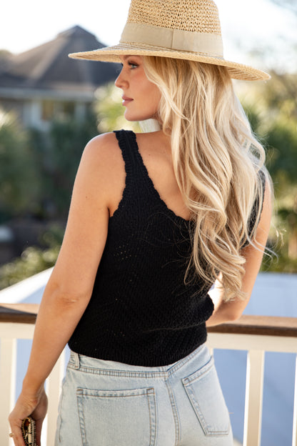 Woman wearing a black sleeveless top and light blue jeans with a straw hat outdoors.