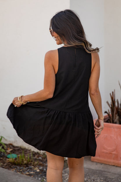 Woman wearing a black dress standing outdoors against a white wall.