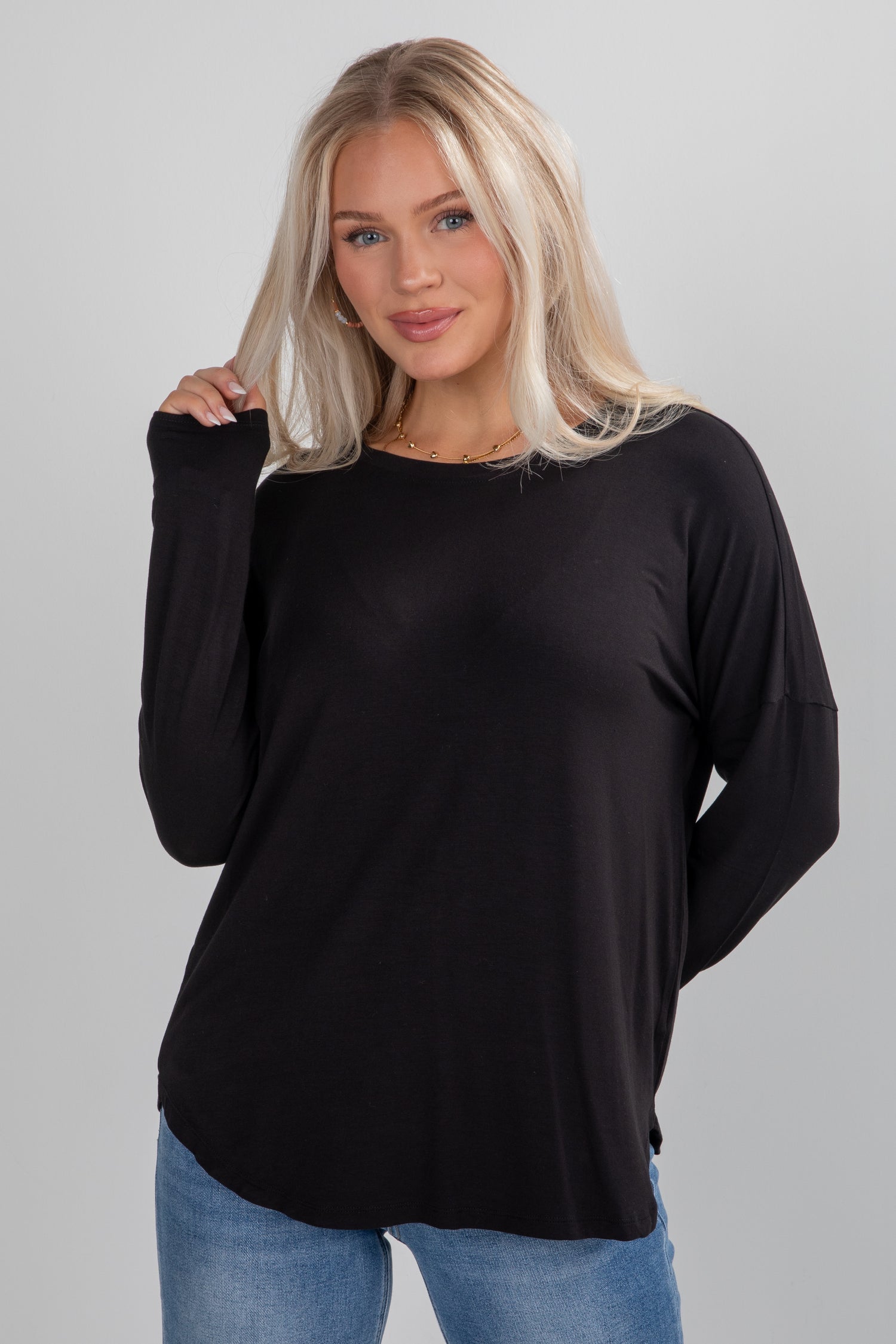 Woman wearing a black long-sleeve top and blue jeans on a gray background