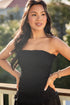 Woman wearing a black strapless dress standing on a balcony with greenery in the background