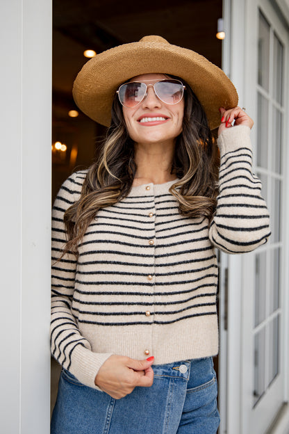 Woman wearing a striped sweater, sunglasses, and a wide-brimmed hat standing indoors.