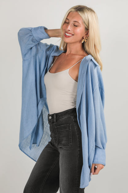 Woman wearing a light blue shirt over a beige tank top and black pants on a plain background