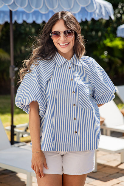 Woman wearing a blue and white striped shirt with sunglasses, standing under a blue umbrella.