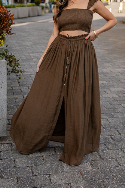 Woman wearing a brown outfit with a long skirt on a paved street.