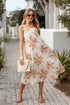 Woman in a floral dress walking outdoors with plants and a building in the background