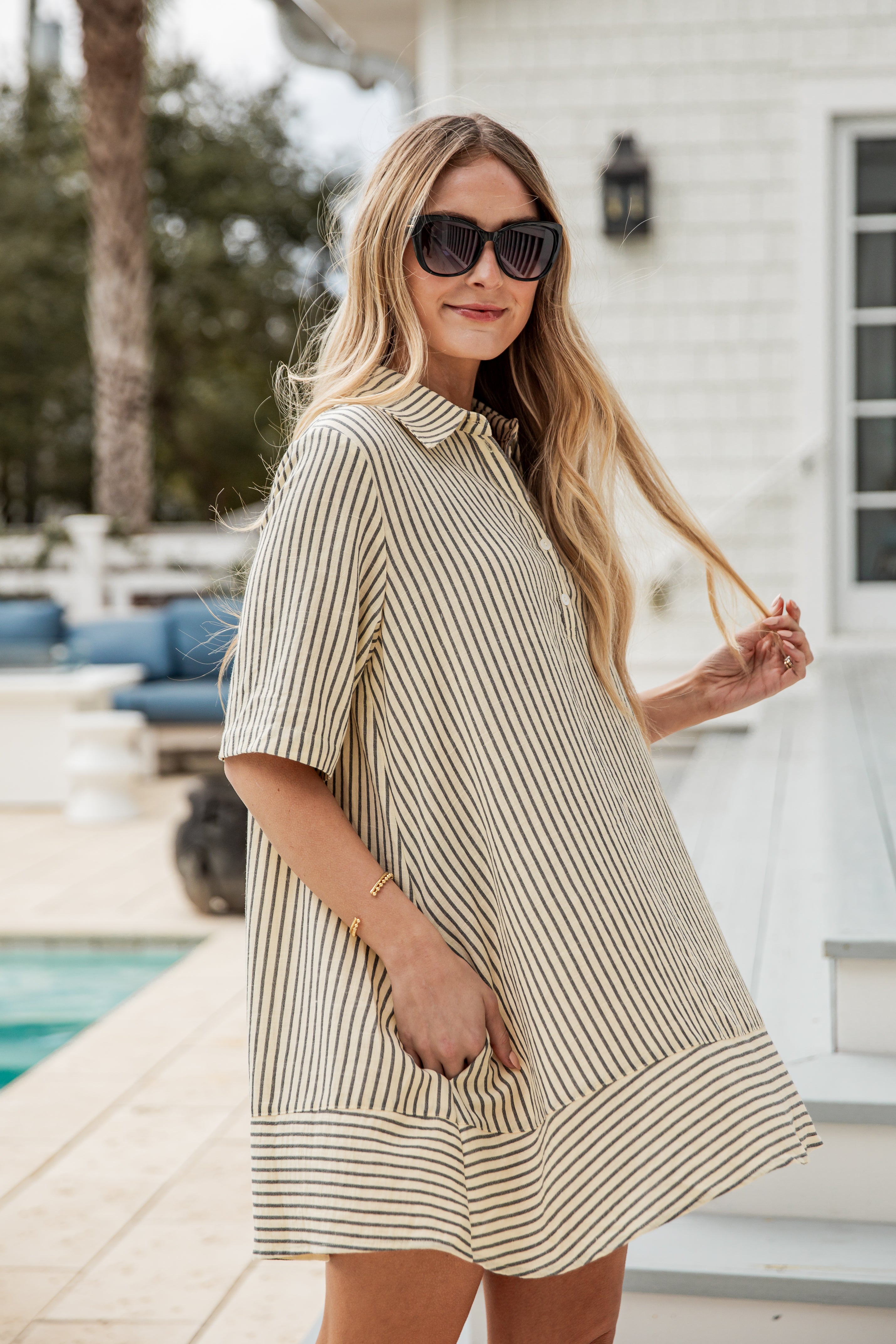 Woman wearing a striped dress and sunglasses by a poolside.