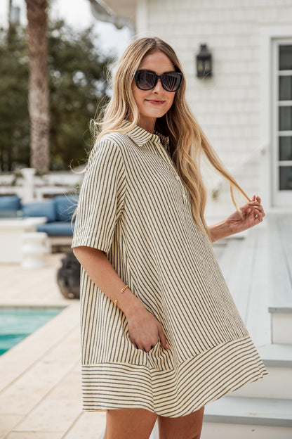 Woman wearing a striped dress and sunglasses by a poolside.