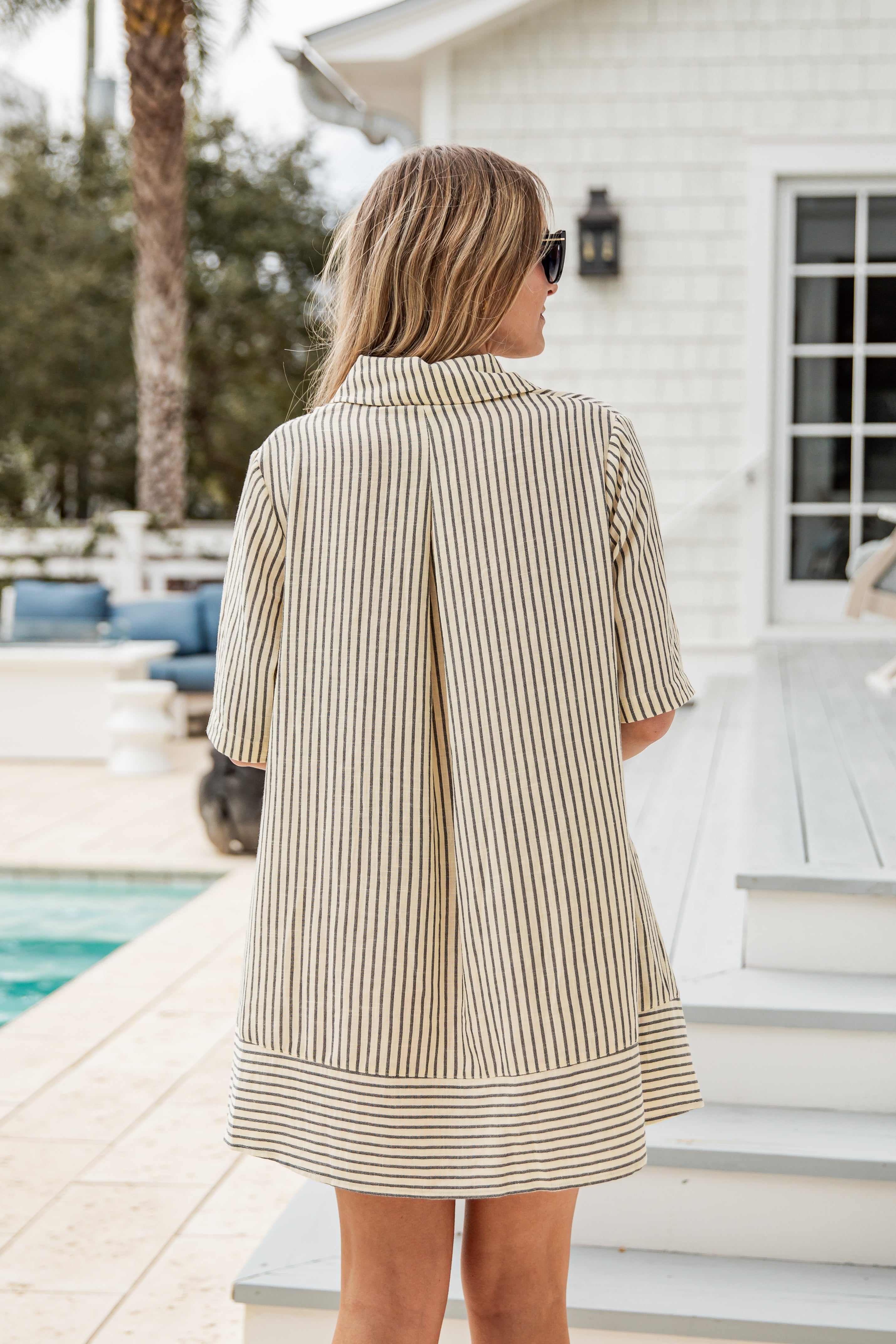 Woman wearing a striped dress standing by a poolside.