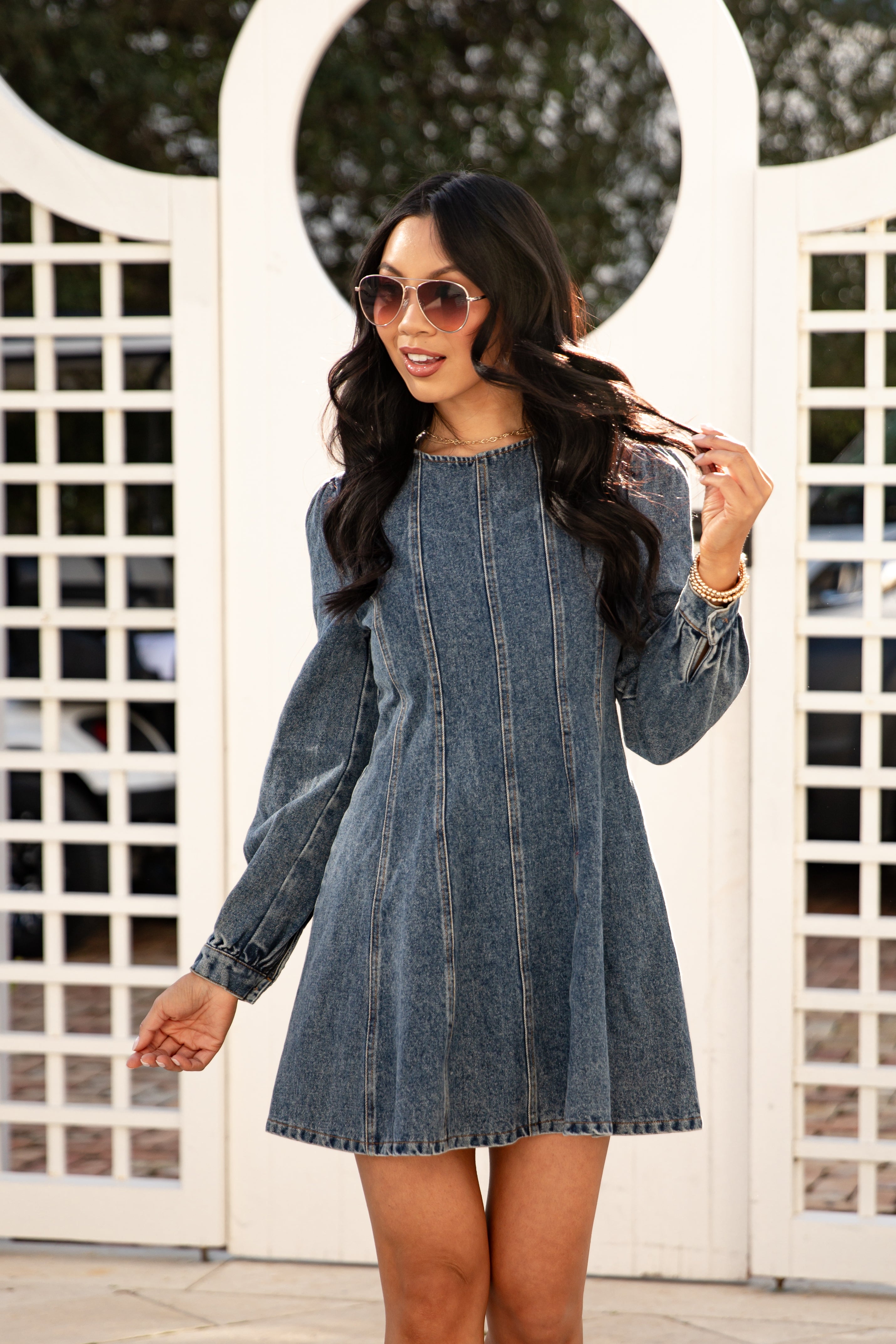 Woman wearing a denim dress in front of a white lattice background