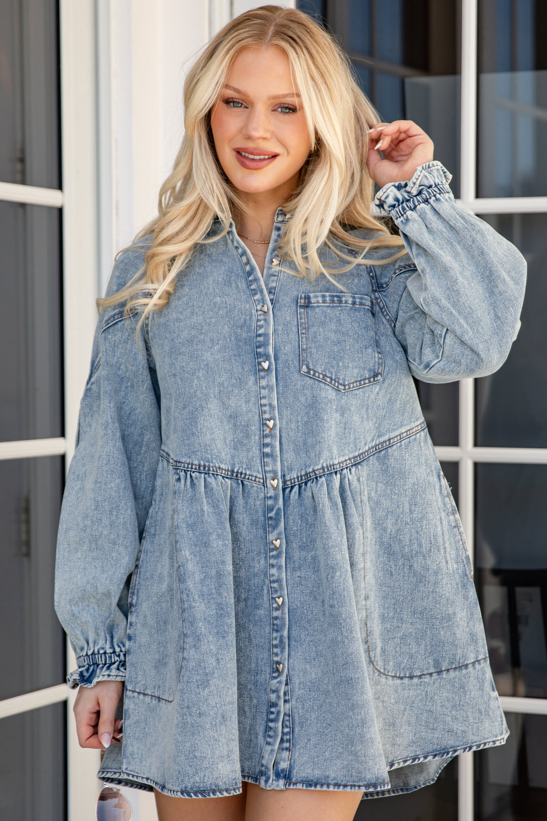 Woman wearing a denim dress standing in front of a glass door.