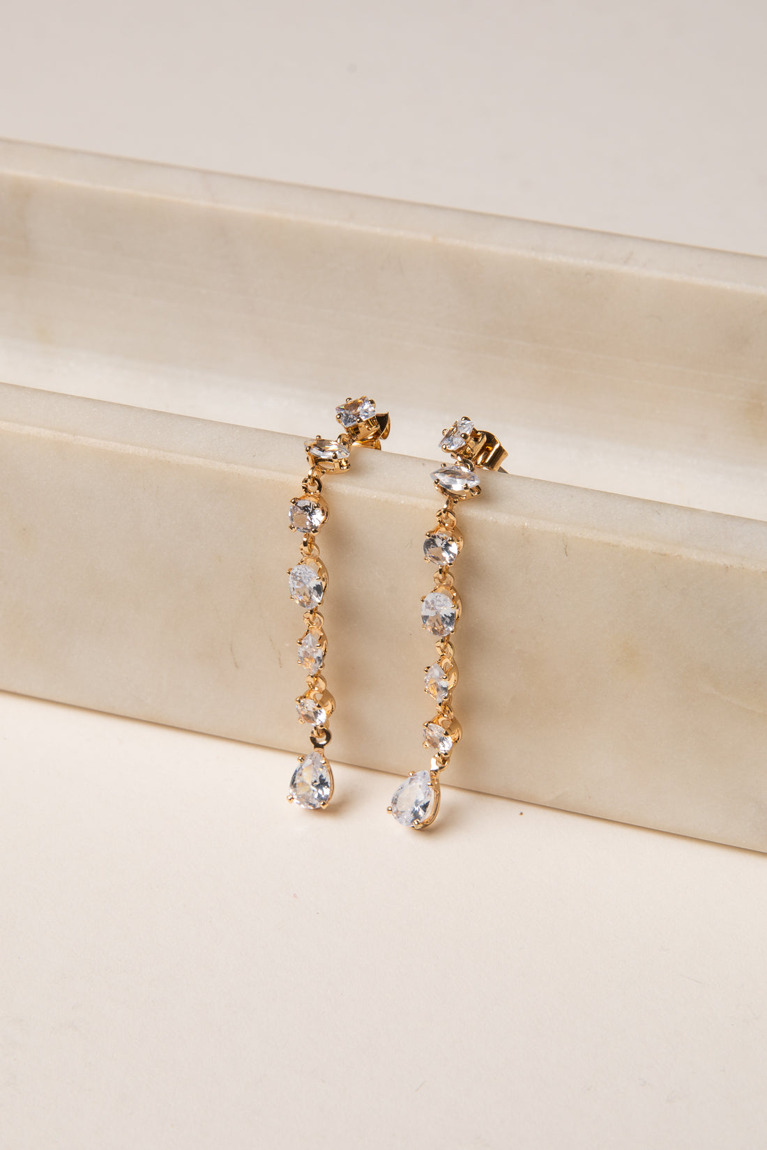 Gold and crystal drop earrings on a beige surface