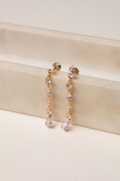 Gold and crystal drop earrings on a beige surface