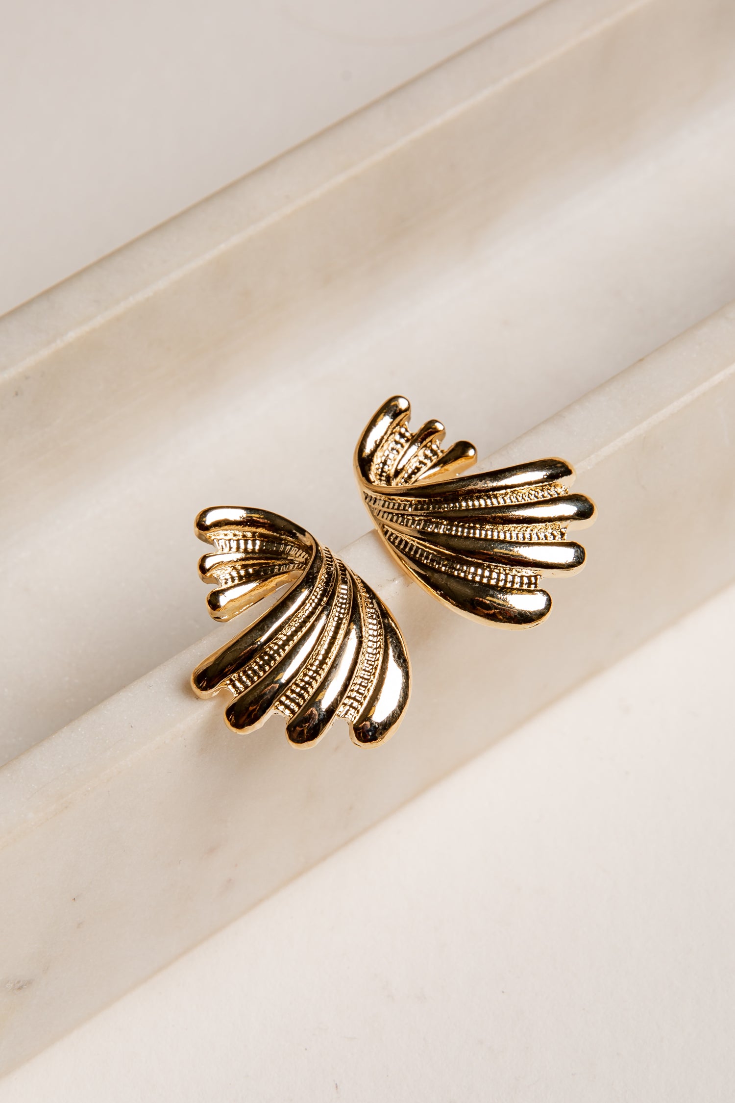 Gold leaf-shaped earrings on a light beige background