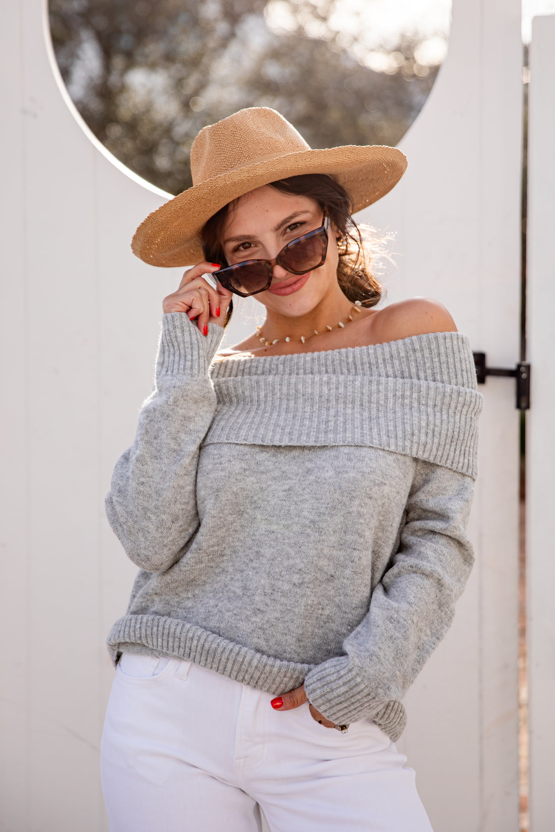 Woman wearing a gray off-shoulder sweater and beige hat, standing outdoors.