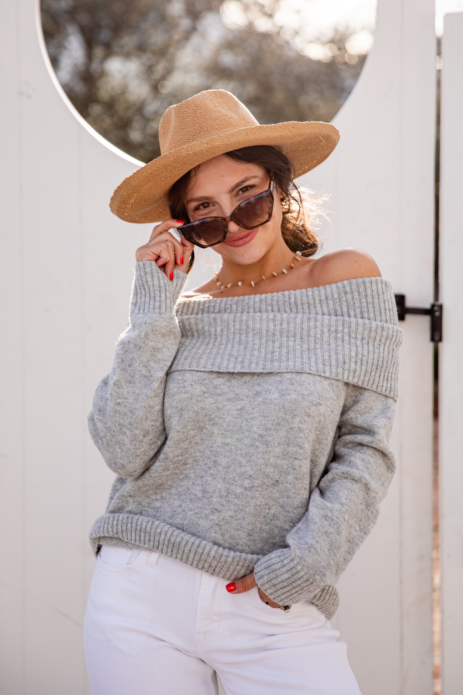 Woman wearing a gray off-shoulder sweater and beige hat, standing outdoors.