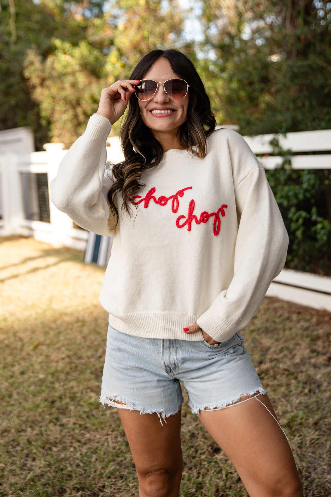Woman wearing a white sweatshirt with red text and light blue shorts outdoors.