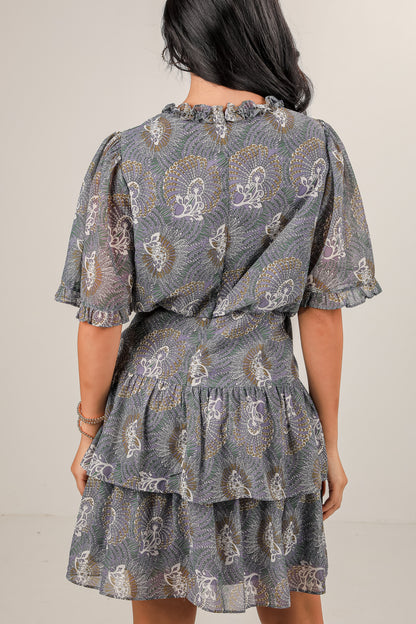 Woman wearing a patterned dress with ruffled layers on a plain background