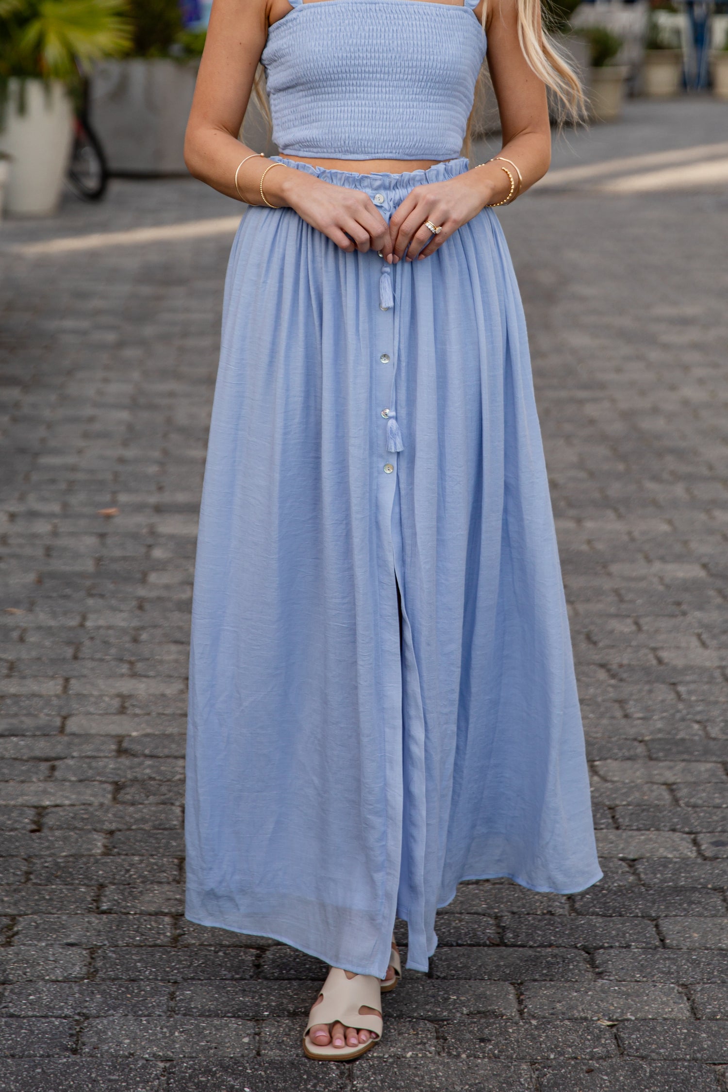 Woman wearing a light blue dress standing on a paved street.