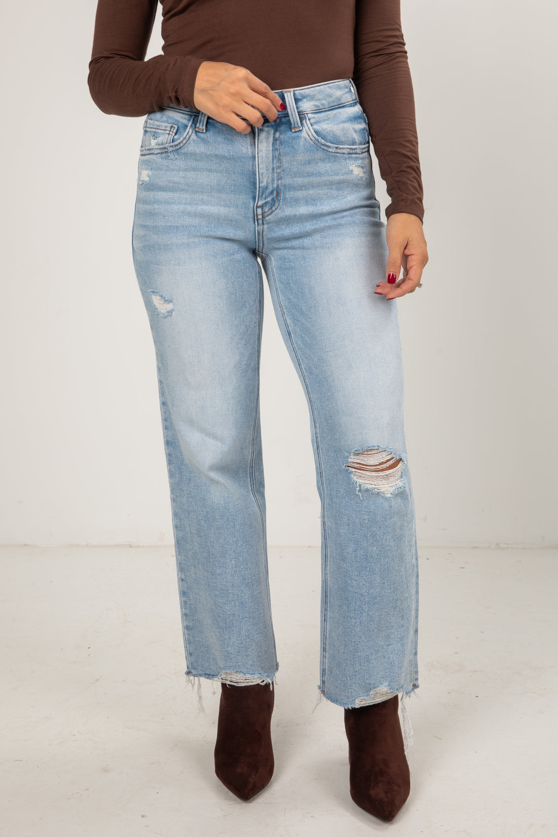 Person wearing light blue jeans and brown top on a white background