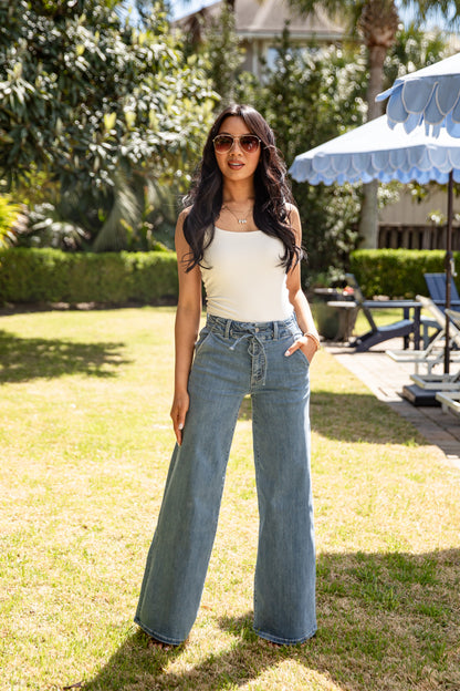Woman wearing a white top and blue jeans standing in a garden.