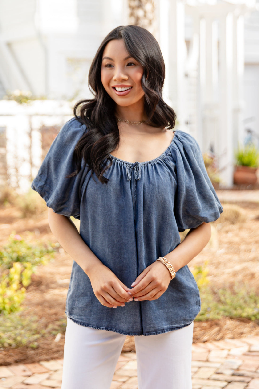 Woman wearing a blue top and white pants standing outdoors.
