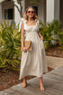 Woman in a white dress standing outdoors with plants and a building in the background