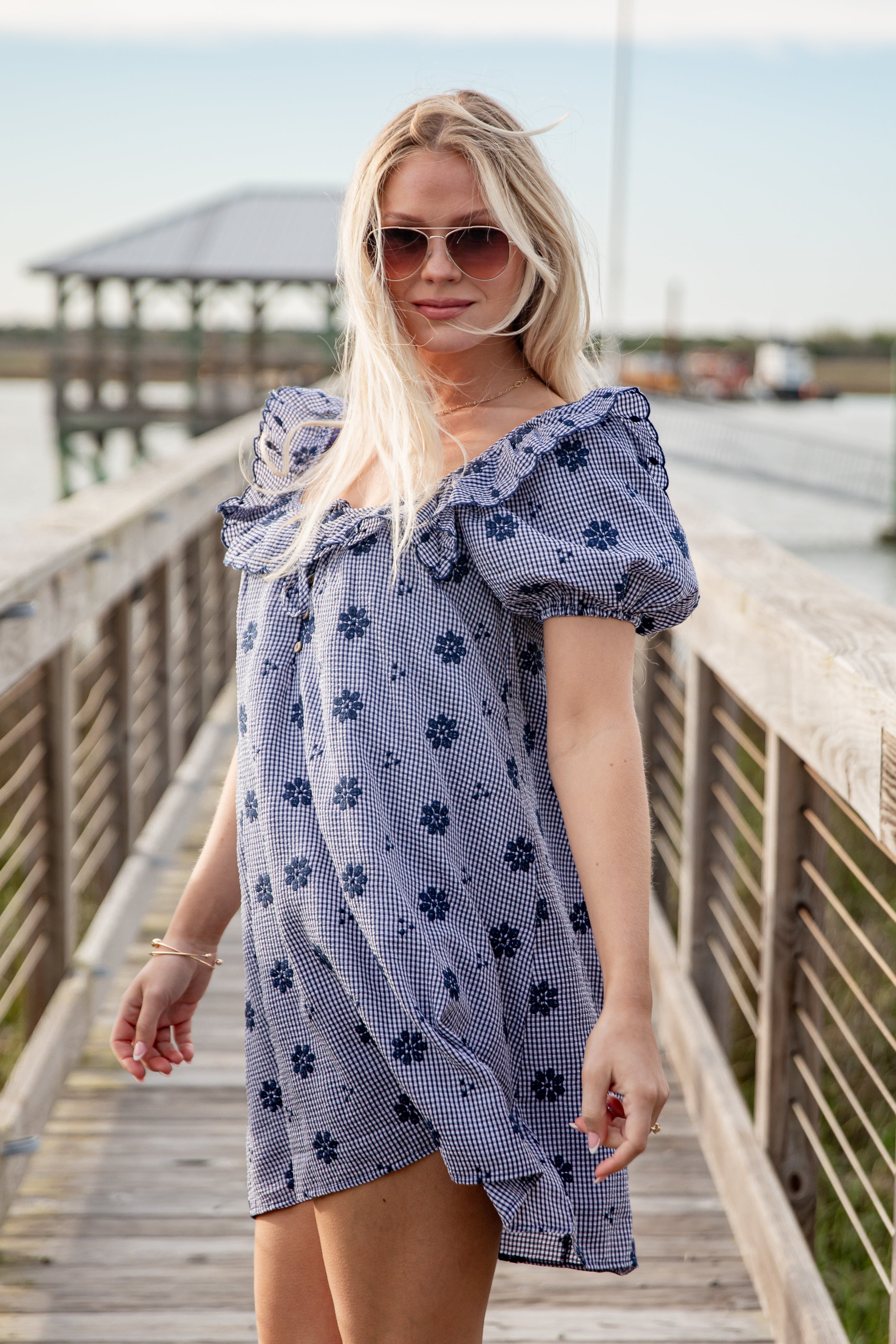 Woman wearing a blue floral dress on a wooden dock by a body of water.