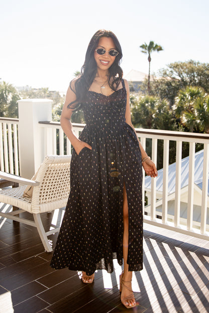 Woman in a black polka dot dress standing on a balcony with greenery in the background