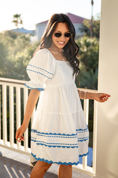 Woman wearing a white dress with blue trim on a balcony