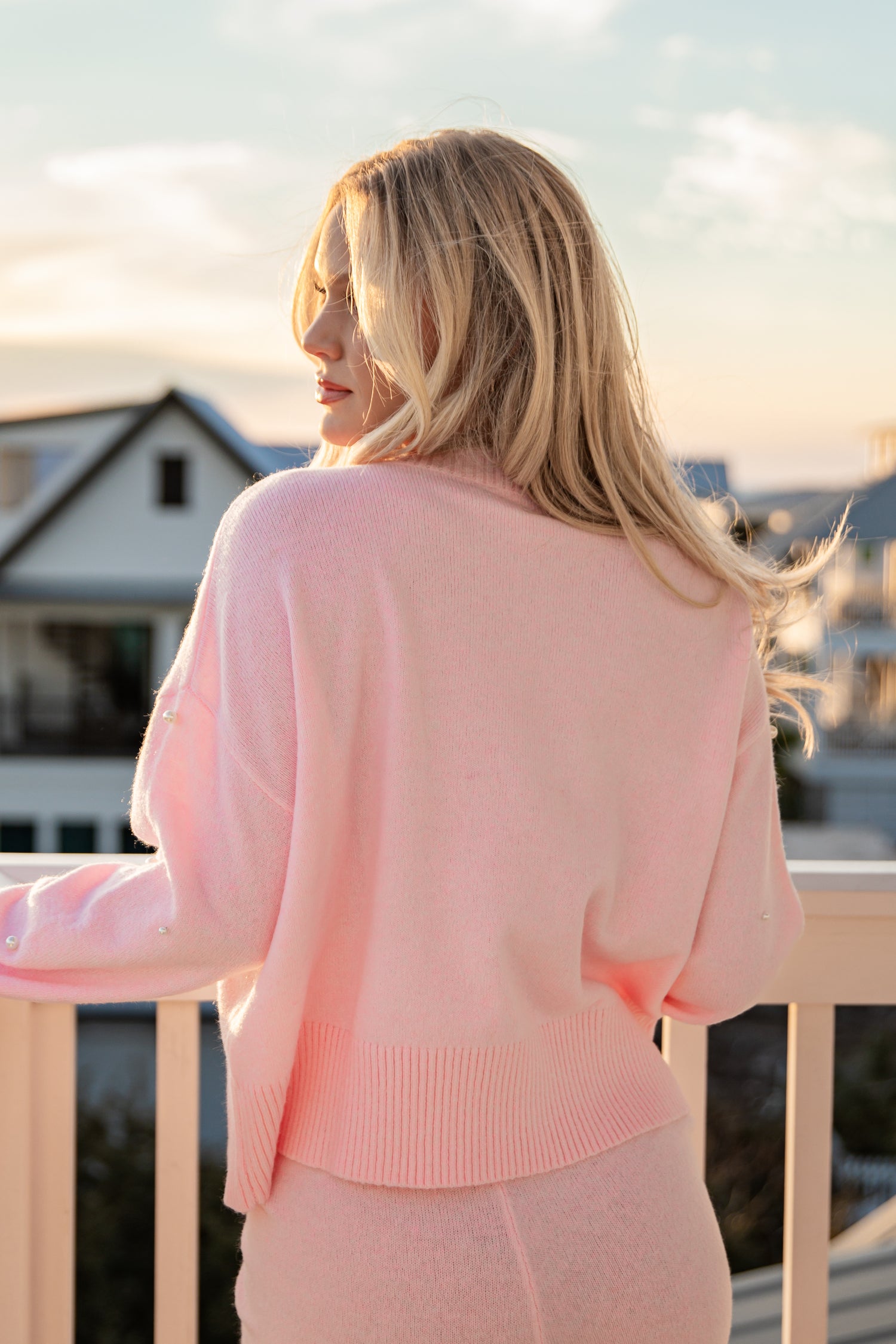Woman wearing a pink outfit standing on a balcony with a scenic background