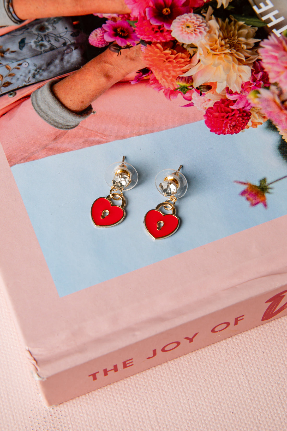 Red heart-shaped earrings on a pink box with flowers in the background