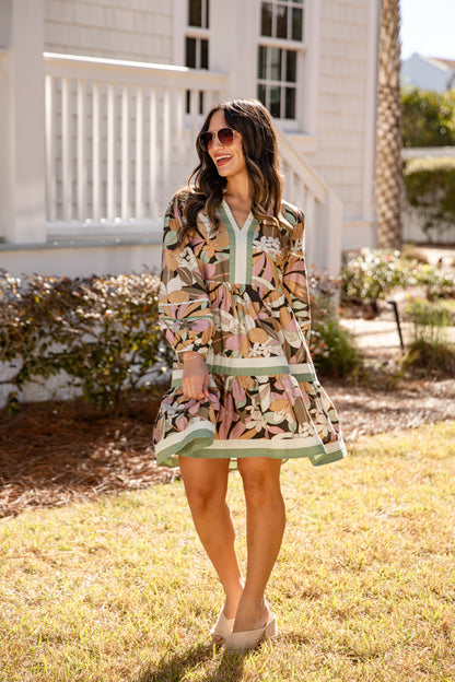 Woman in a patterned dress standing outdoors with a house in the background