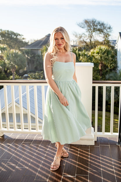 Woman in a light green dress standing on a balcony with trees in the background