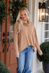 Woman wearing a beige sweater and blue jeans standing in front of a door with Christmas decorations.