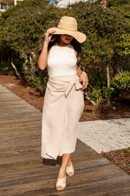 Woman wearing a white top and beige skirt with a straw hat on a wooden path.