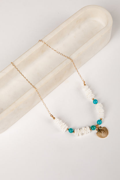 Necklace with white beads, turquoise stones, and a gold shell pendant on a marble surface.