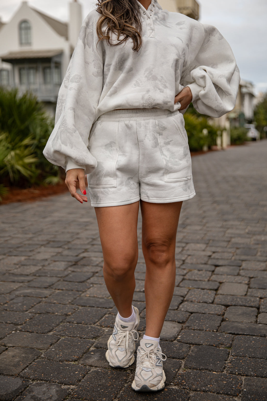 Person wearing a light gray outfit with shorts and sneakers on a paved walkway.