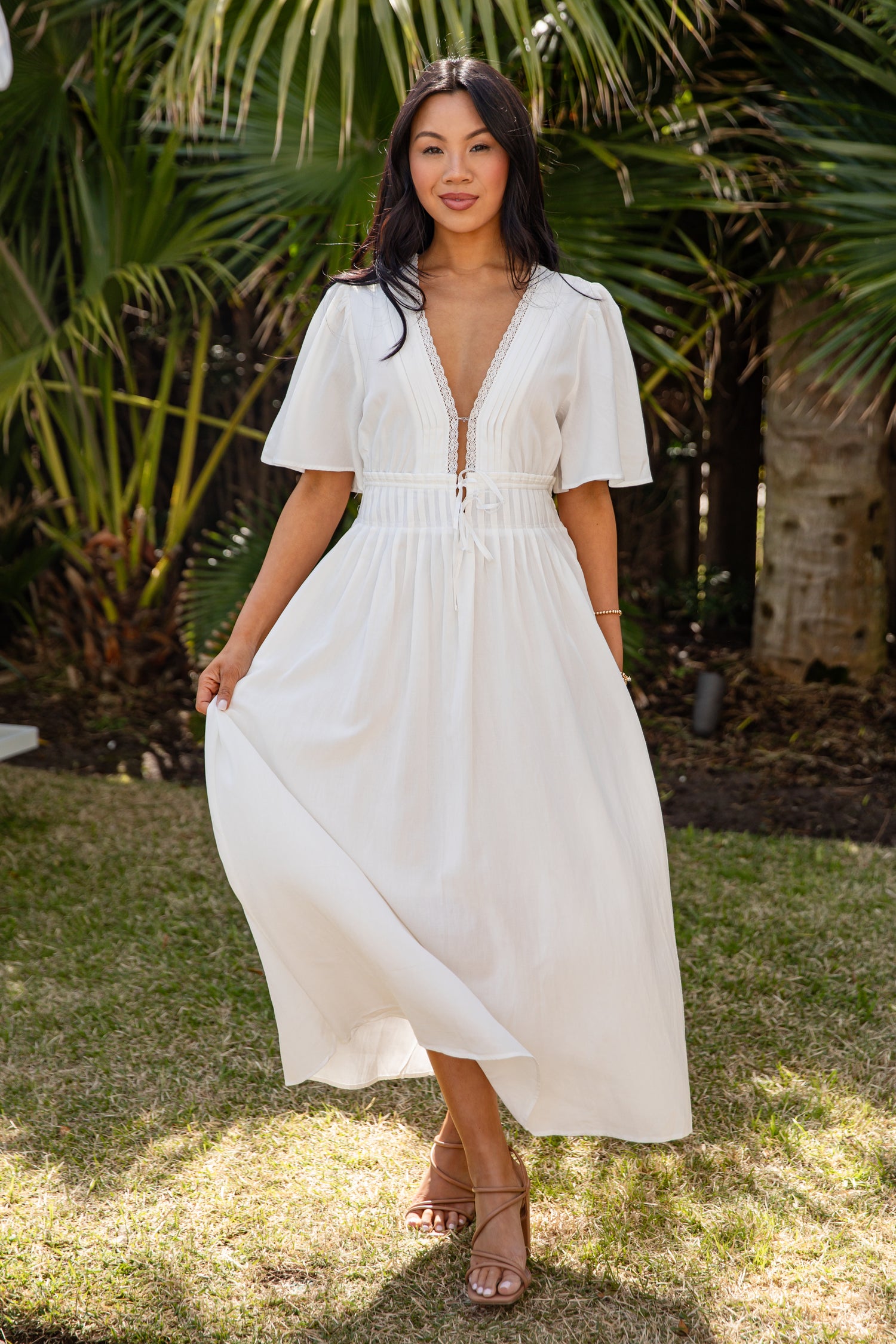 Woman in a white dress standing outdoors with greenery in the background