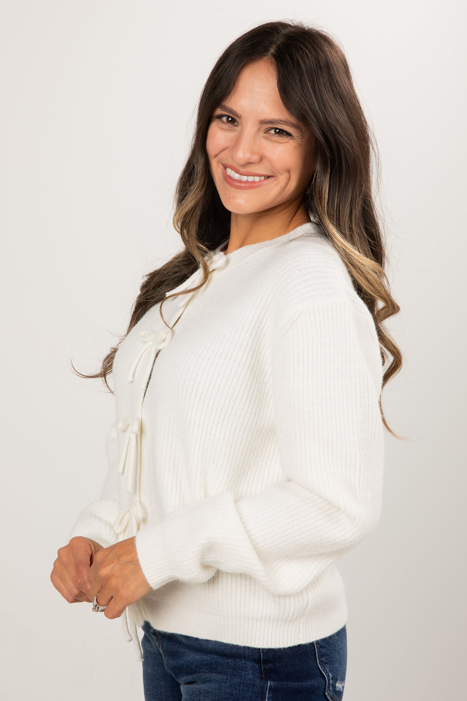 Woman wearing a white sweater and blue jeans against a plain background