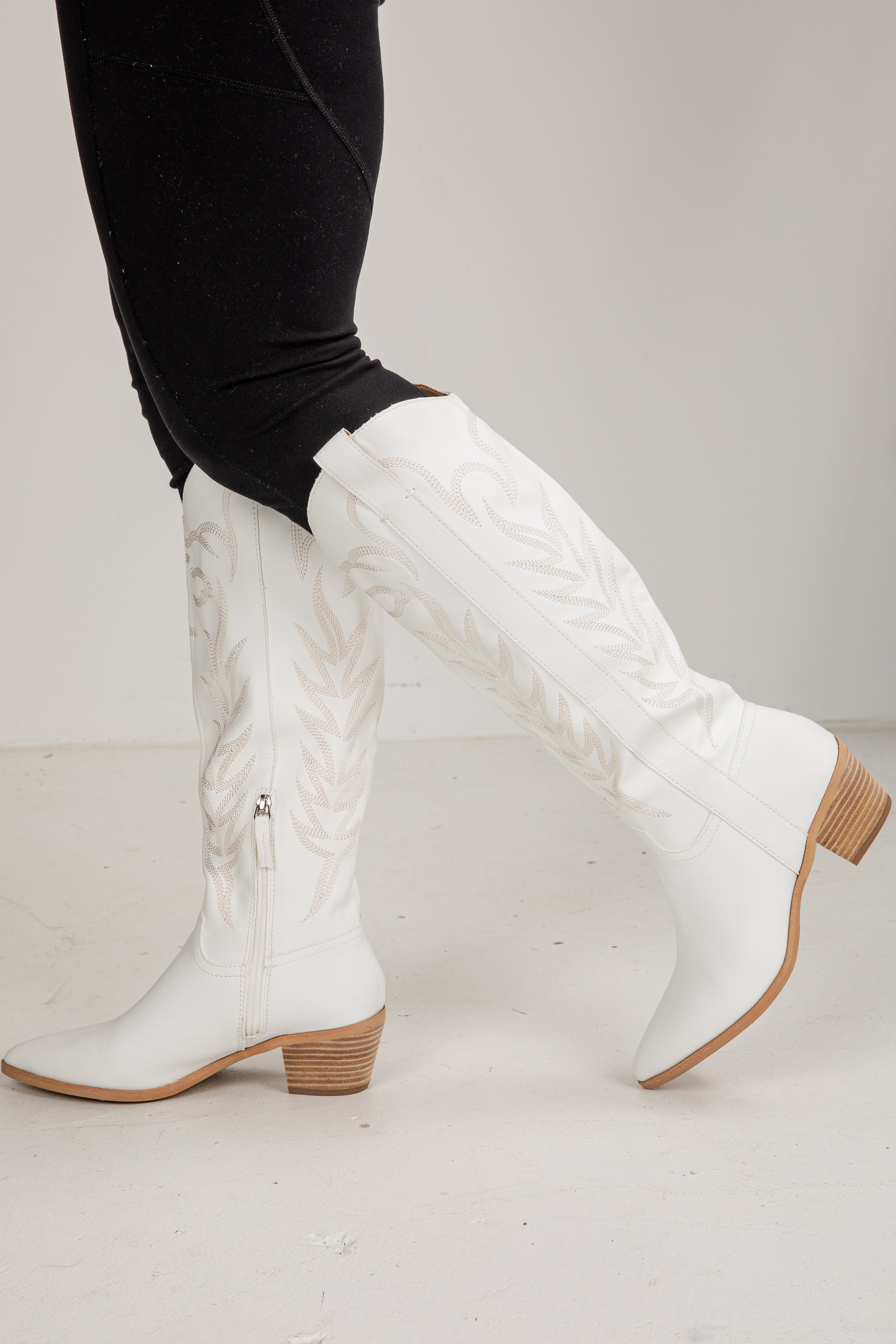 White knee-high boots with brown soles worn by a person on a light gray background