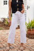 Person wearing a black top with gold buttons and white pants standing on a brick patio.
